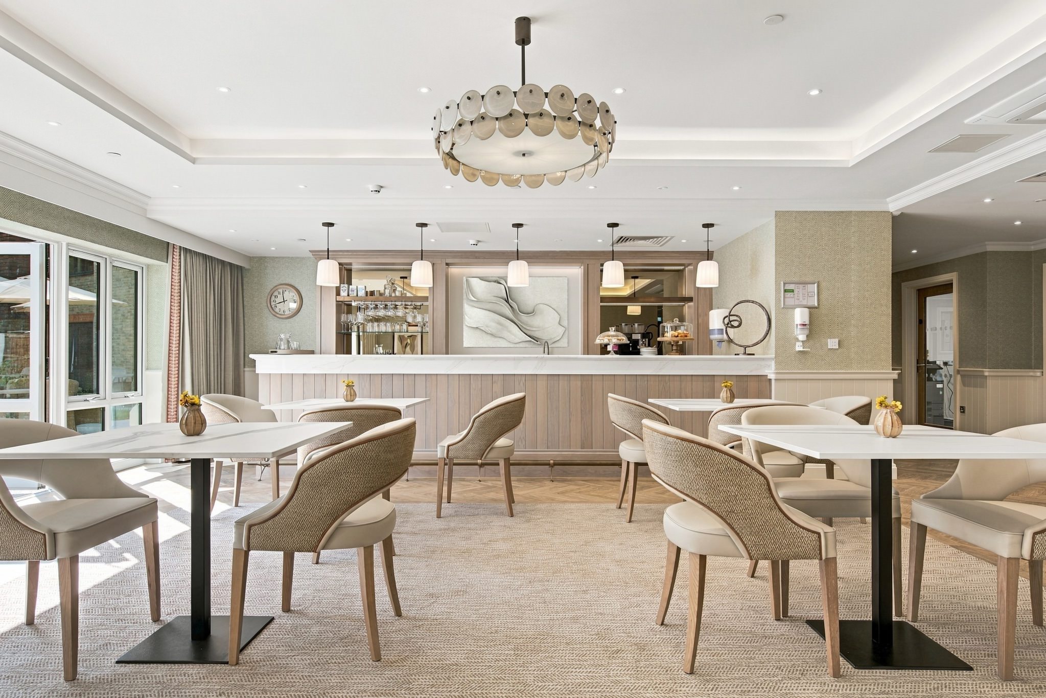 Bistro and bar area at Kings Hill Care Home with marble-topped tables, upholstered chairs and pendant lights.