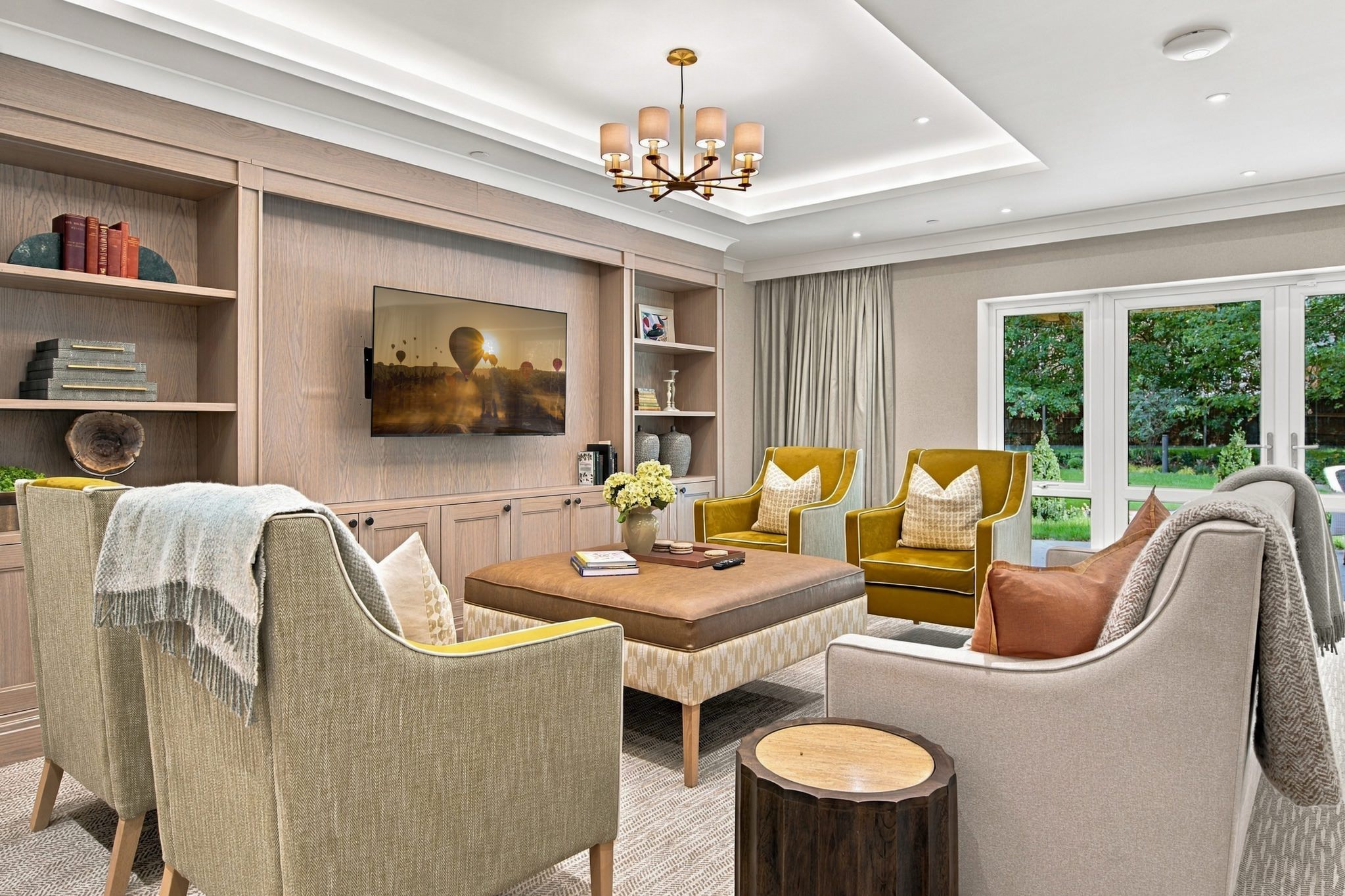 Care home photography of the lounge at Kings Hill Care Home, with mustard velvet armchairs, a leather ottoman and French doors onto the garden.