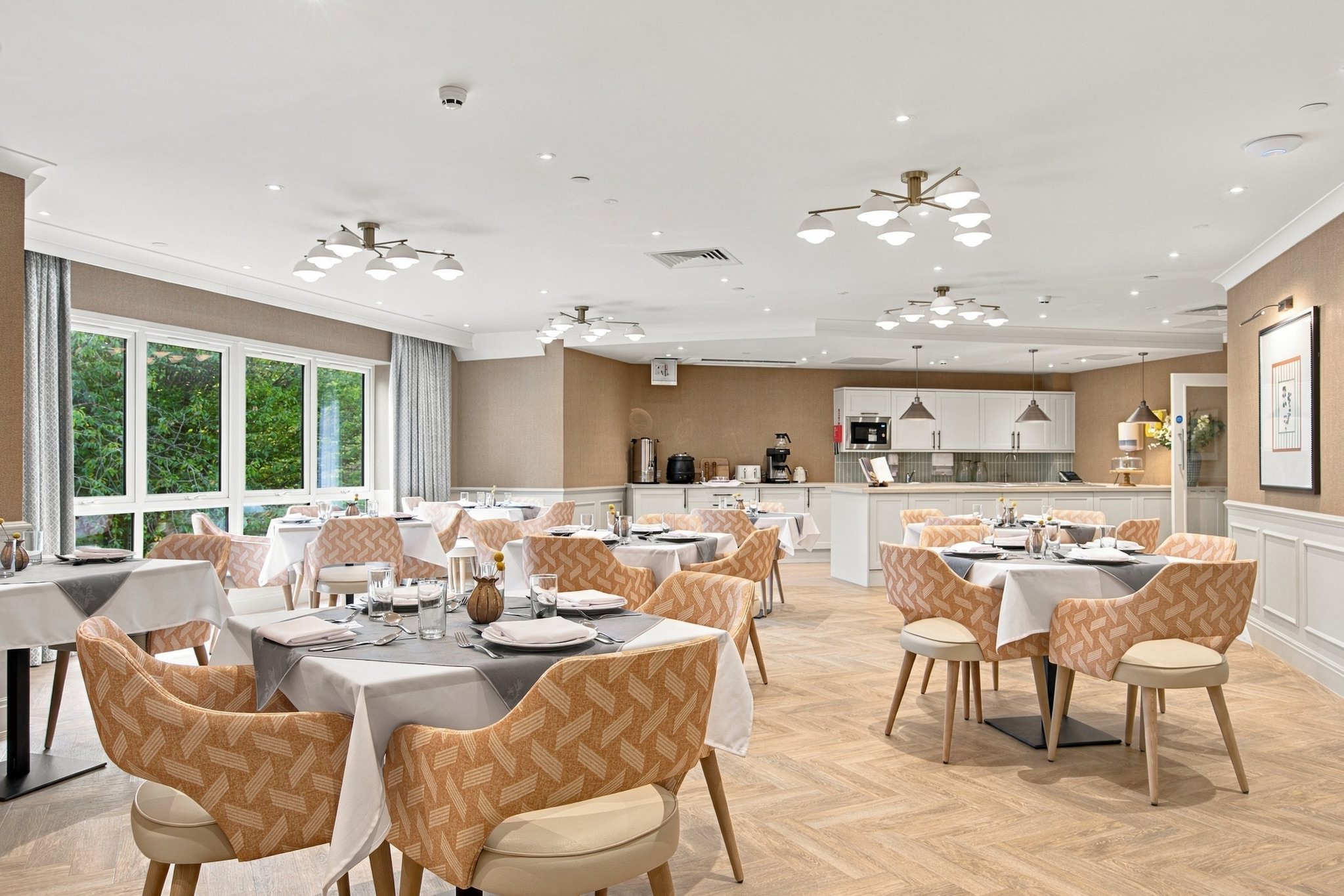 Main dining room with tables laid for lunch, peach patterned chairs and herringbone flooring.
