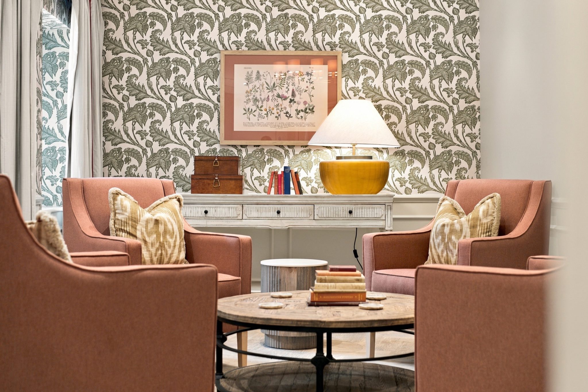 Cosy seating area with terracotta armchairs, botanical wallpaper and a framed botanical print.